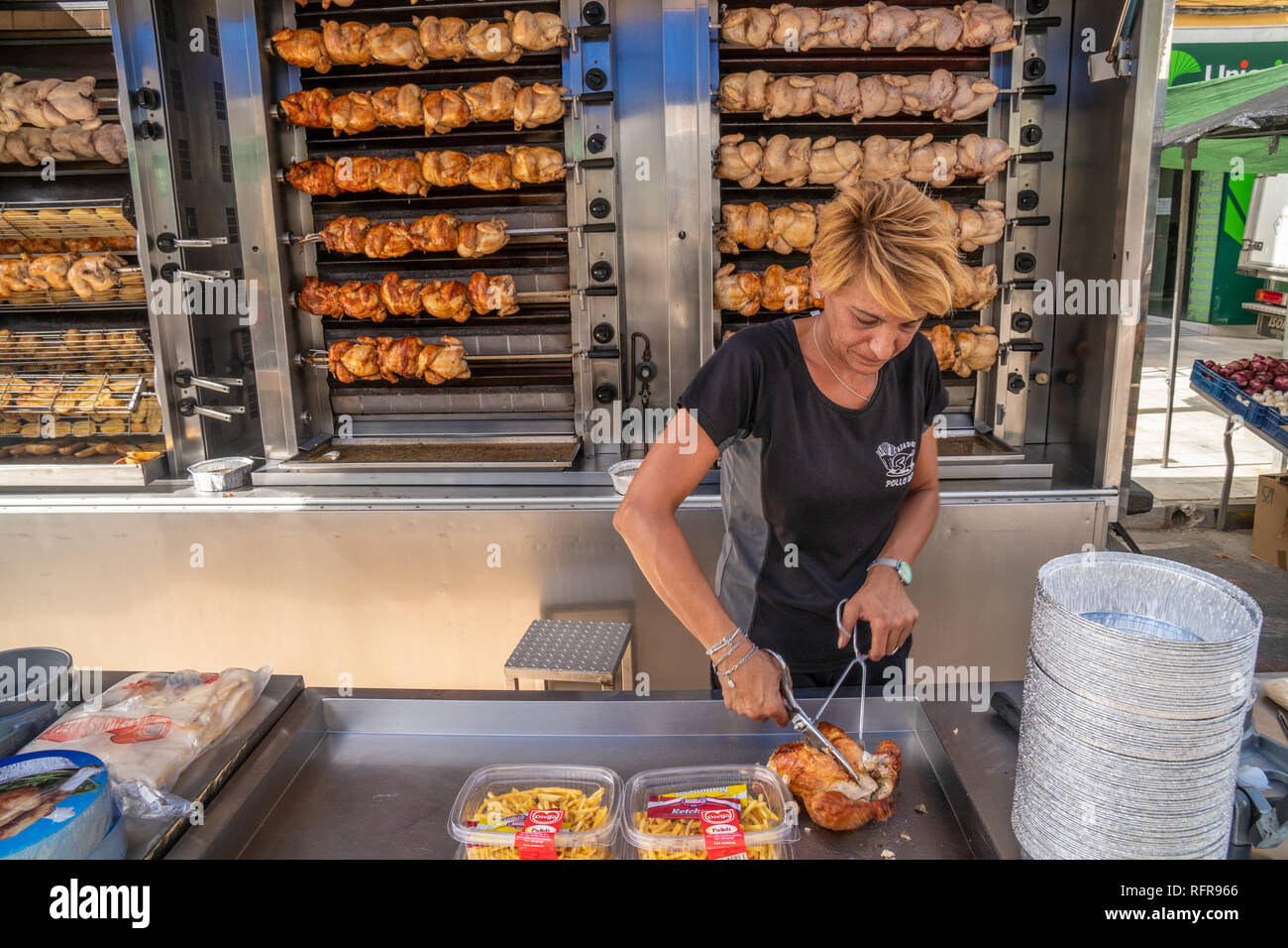 La donna la preparazione di pasti da asporto infront di polli essendo spiedo sul lato di un furgone nel mercato spagnolo Foto Stock