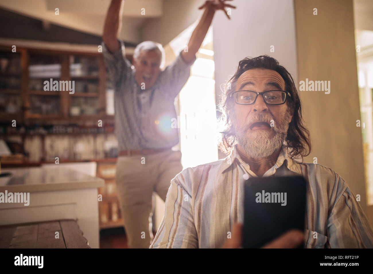 Senior uomo prendendo selfie con un amico in piedi sul retro compiendo gesti selvatici. Cray anziani uomo rendendo ritratto di auto a casa. Foto Stock