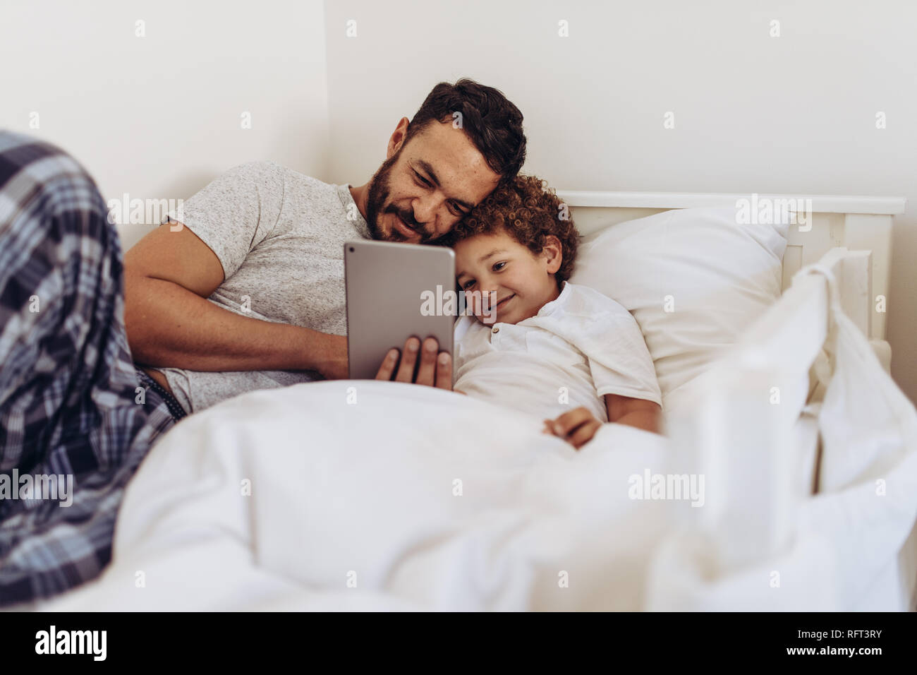 Padre e figlio sdraiato sul letto a guardare un film sul tablet pc. Uomo disteso sul letto con il suo ragazzo tenendo un tablet pc in mano. Foto Stock