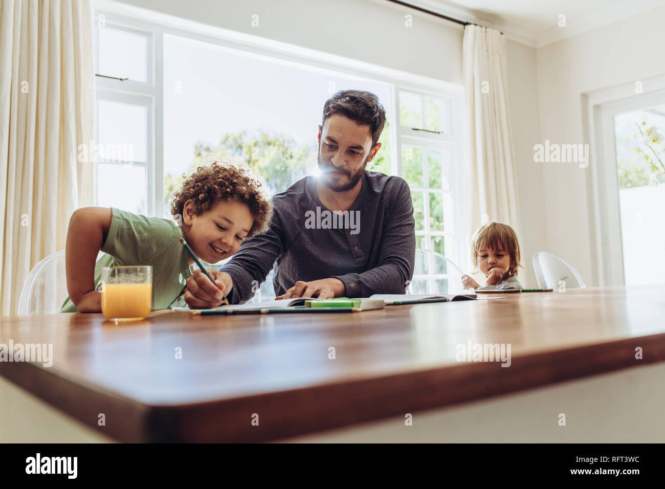 Uomo seduto a tavola a casa con i suoi bambini di prendersi cura di loro. Padre aiutando il suo figlio nei suoi studi. Foto Stock