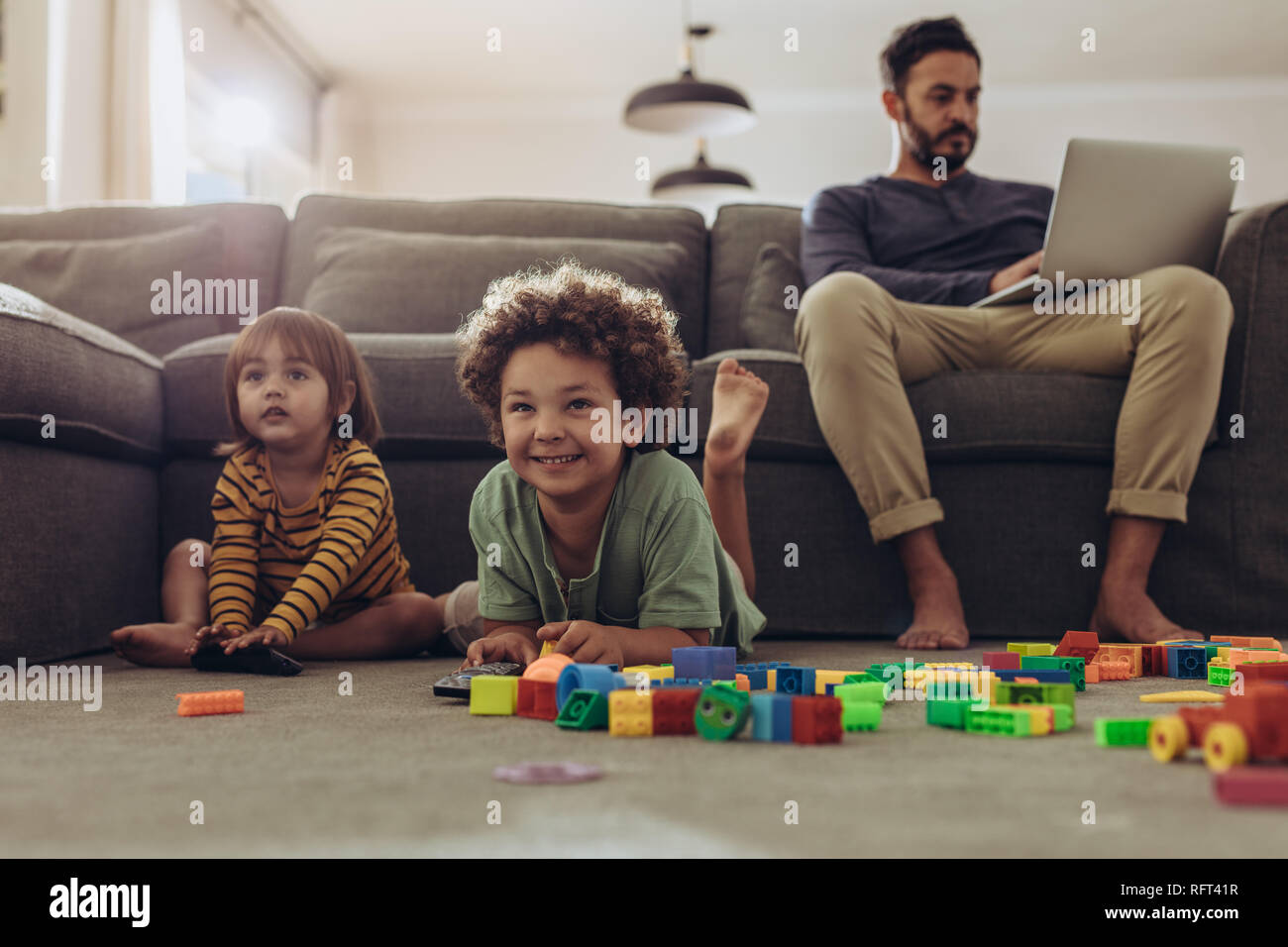 Sorridere i bambini giocando con la costruzione di blocchi e guardare la televisione a casa. L'uomo baby i suoi bambini e lavora da casa. Foto Stock