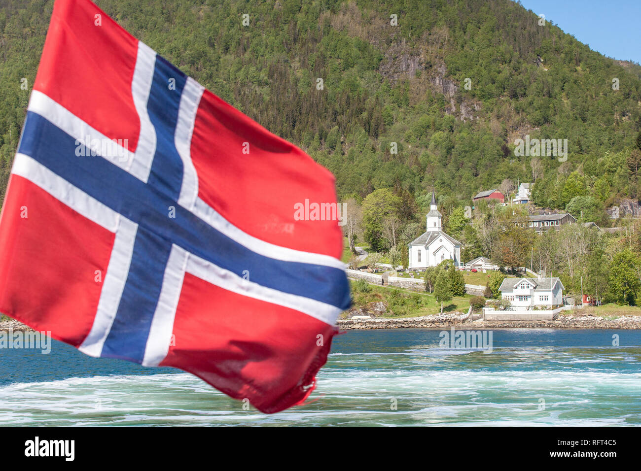 Chiesa di legno dal fiordo con bandiera norvegese, Sognefjord, Norvegia Foto Stock