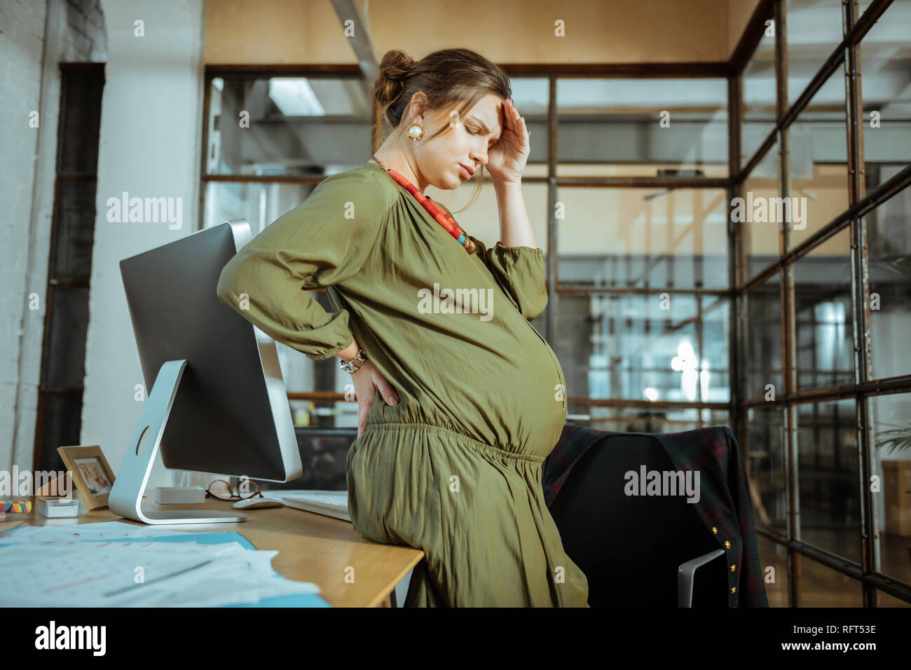 Dai capelli scuri donna incinta indossando abiti cachi avente mal di testa Foto Stock