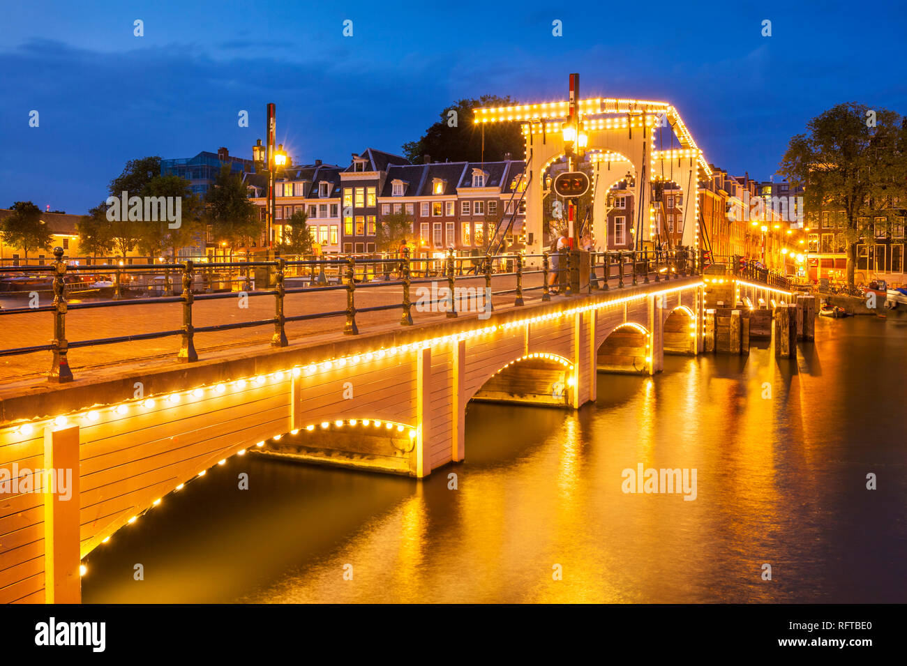 Illuminata Magere Brug (Skinny Bridge) di notte che attraversano il fiume Amstel di Amsterdam, Olanda Settentrionale, Paesi Bassi, Europa Foto Stock