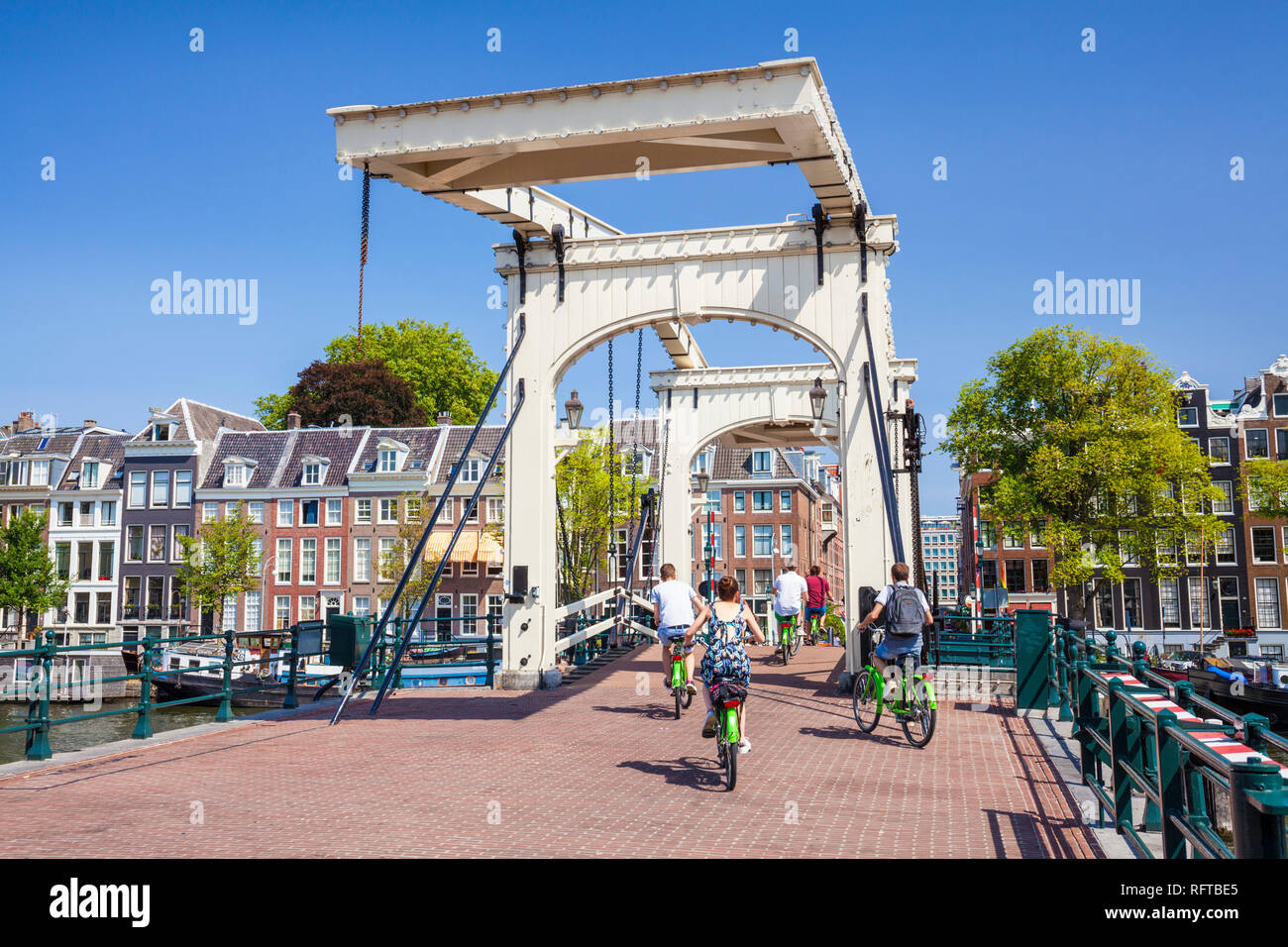 I ciclisti in sella attraverso il Magere Brug (Skinny Bridge) che attraversano il fiume Amstel di Amsterdam, Olanda Settentrionale, Paesi Bassi, Europa Foto Stock