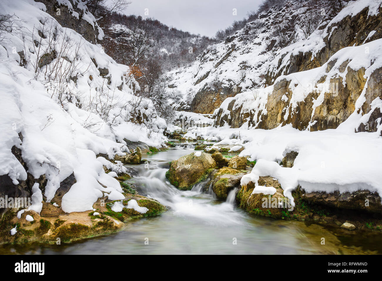 I colori vivaci di una mountain creek cascading attraverso il canyon coperto di neve Foto Stock