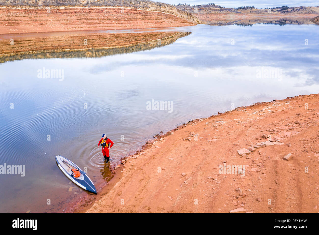 Vista aerea di un stand up paddler in una drysuit sulla riva del lago, tipico paesaggio invernale nel nord Colorado pedemontana con assenza di neve e di basso livello acqua Foto Stock