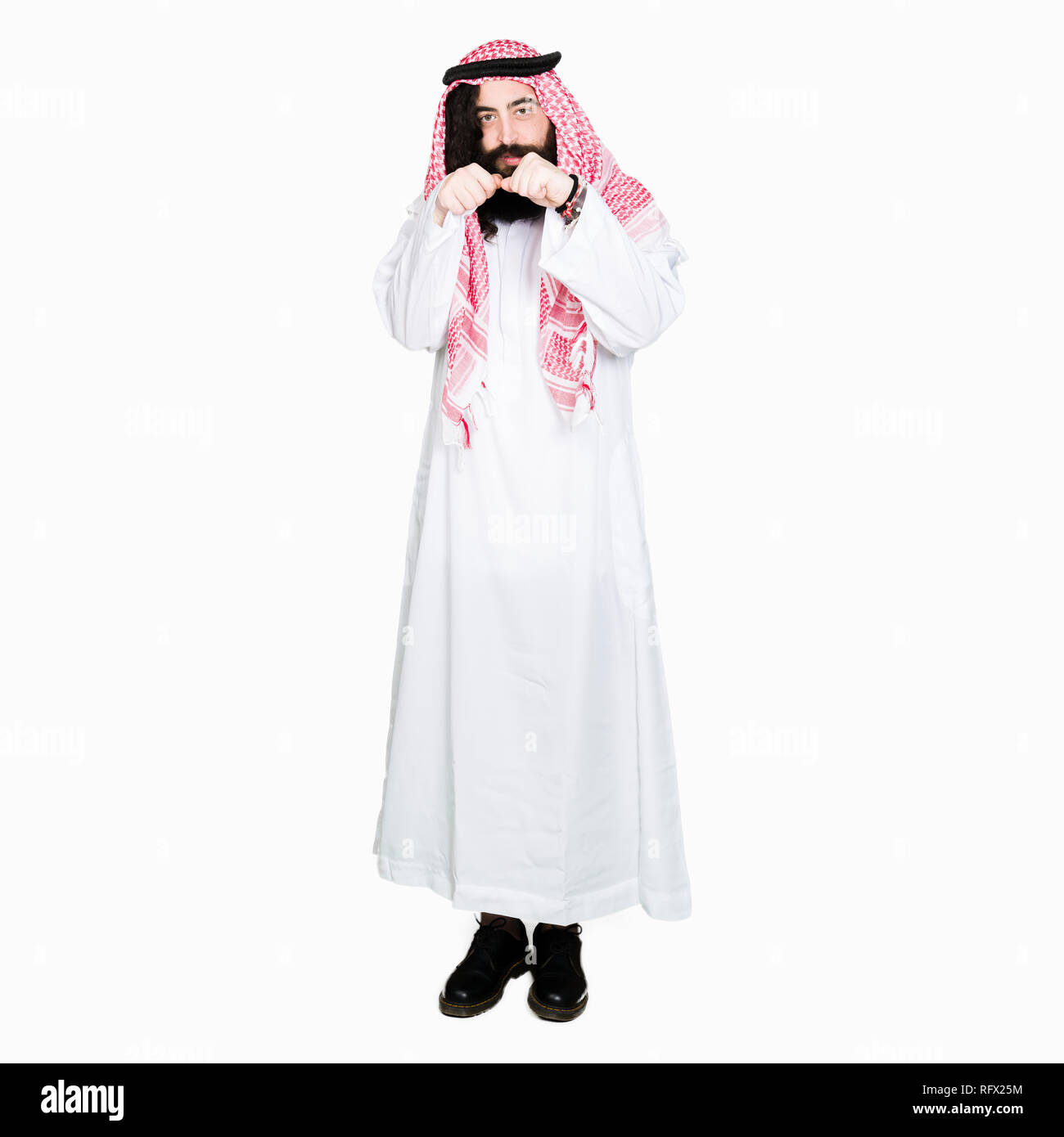 Arabian business man con capelli lunghi indossando il tradizionale keffiyeh sciarpa pronti a lottare con pugno gesto di difesa, arrabbiato e sconvolto il viso, paura di probl Foto Stock