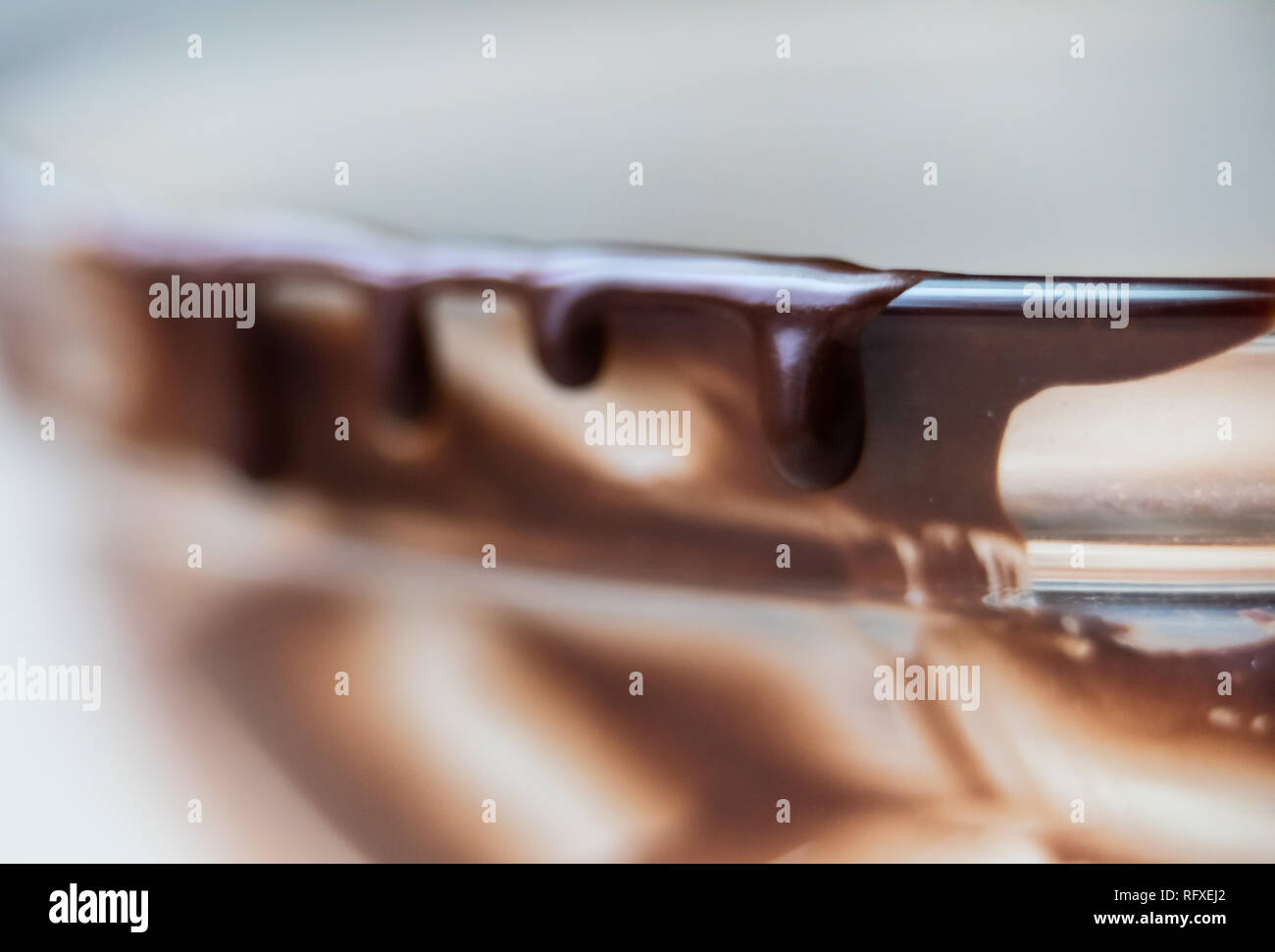 Macro closeup di liquido cremoso liscio marrone scuro di sciroppo al cioccolato glassa in recipiente di vetro isolato di sgocciolamento bordo lati Foto Stock