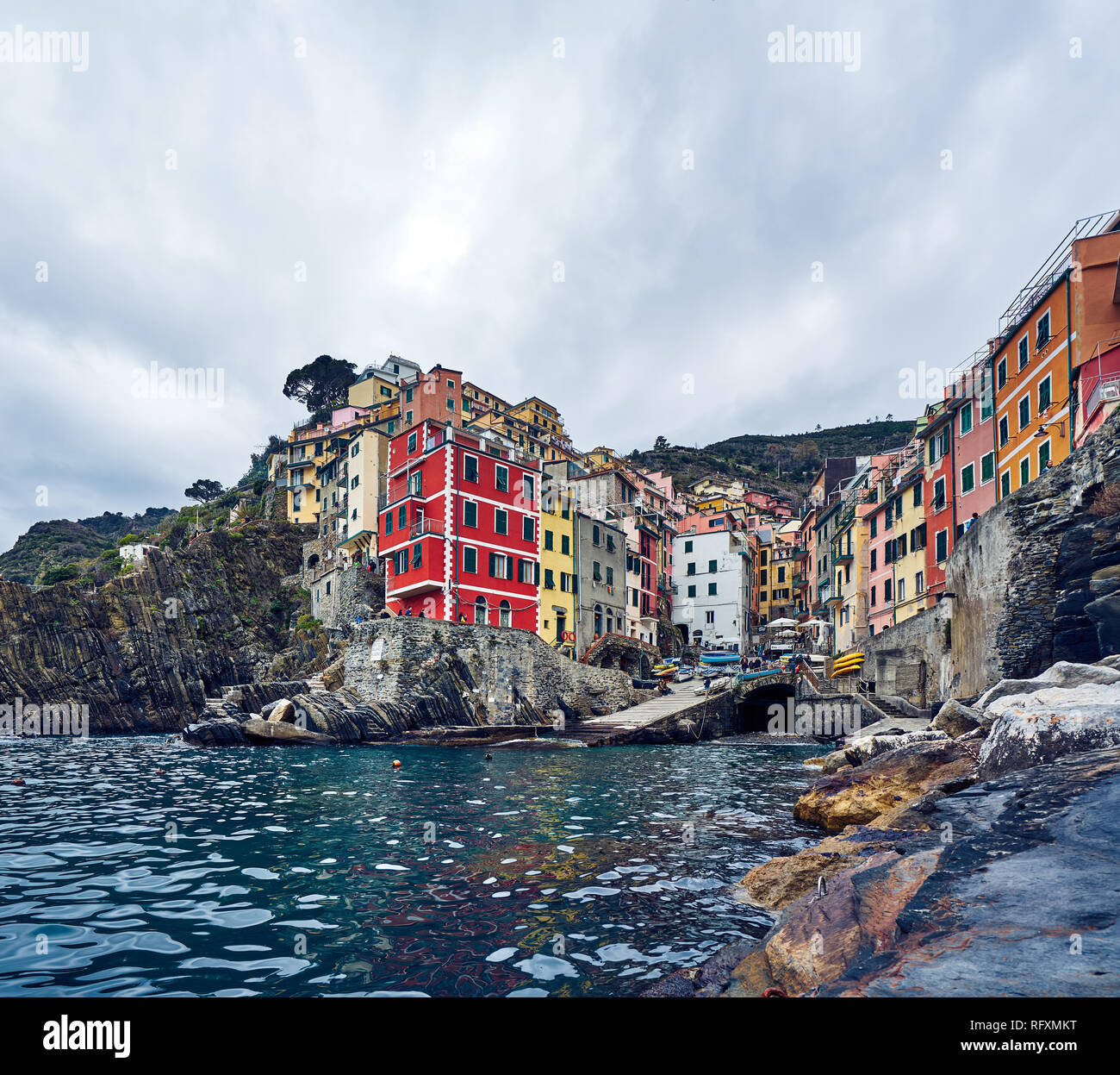 Riomaggiore è il primo arresto su molti Cinque Terre visite. Peeling linea edifici verso il basso di un ripido burrone per un piccolo porto. Foto Stock