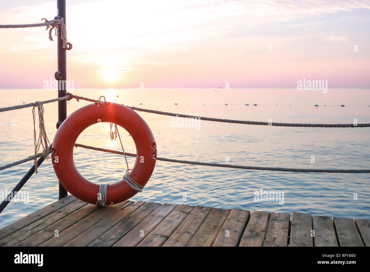 Lifebelt rosso sul molo in legno sullo sfondo di paesaggi marini all'alba. Foto Stock