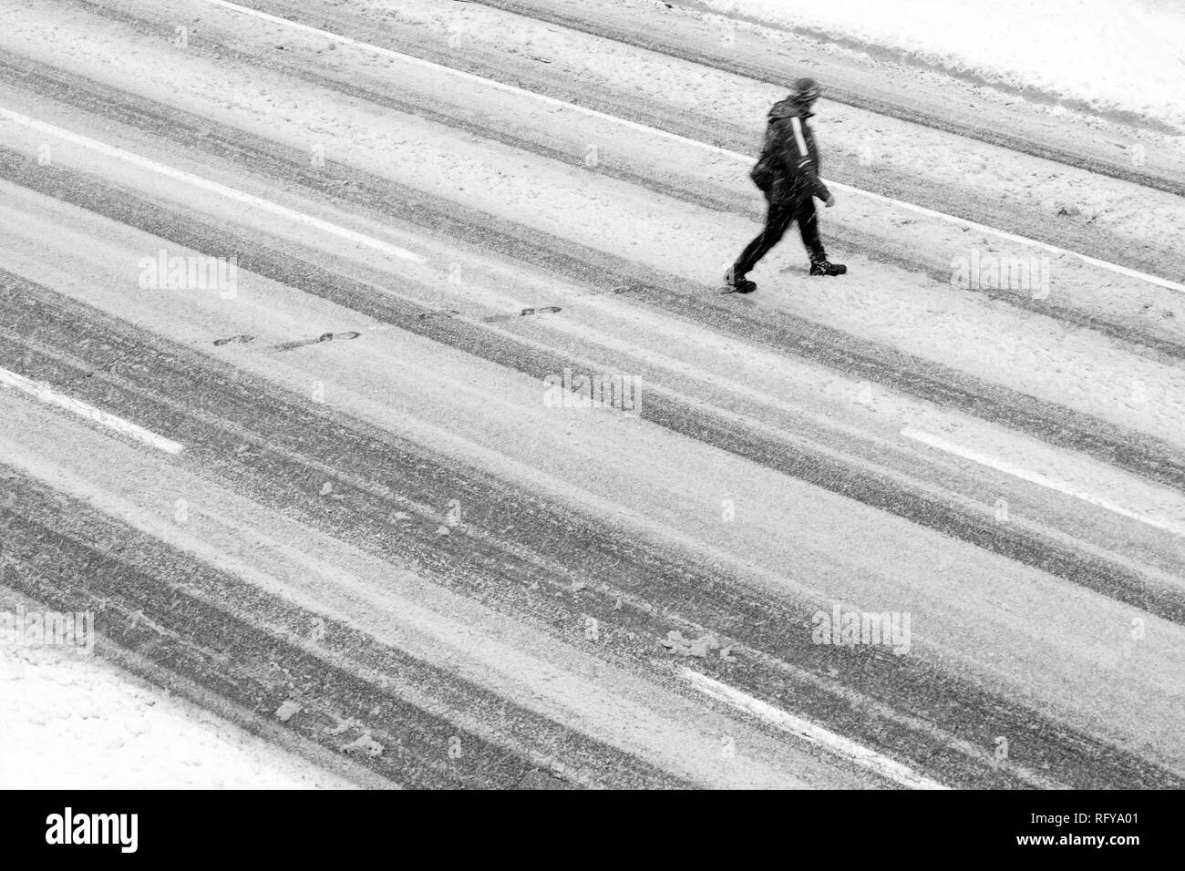 Un uomo che attraversa la strada vuota durante la tempesta di neve, ad alto angolo di visione in bianco e nero Foto Stock