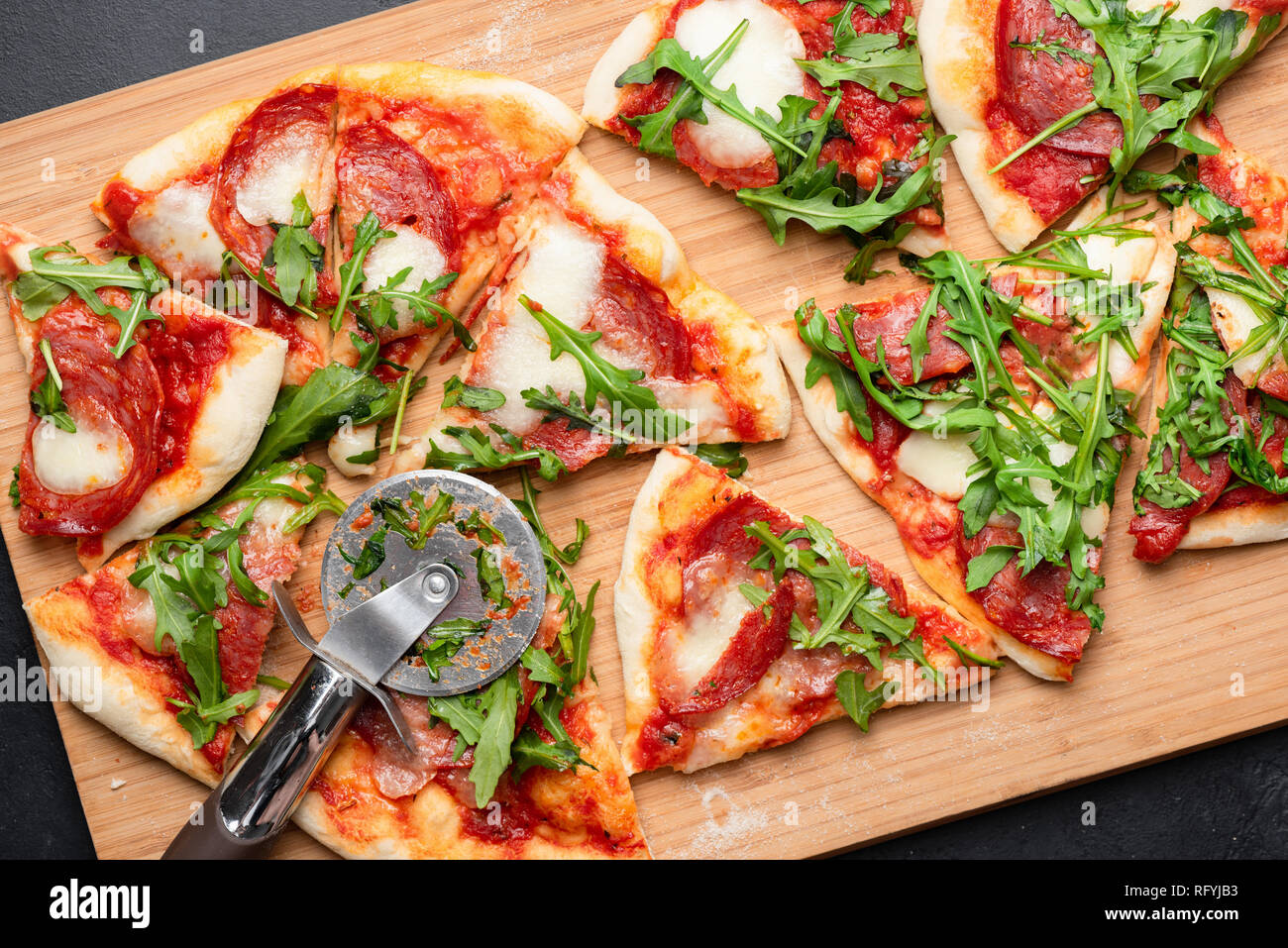 Pizza con salame, mozzarella e salsa di pomodoro guarnita con foglie di rucola. Fette di pizza. Tabella vista superiore Foto Stock