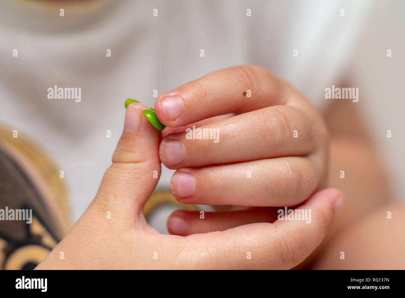 Un giovane bambino con le mani in mano a giocare con e mangiare piselli a ora di cena Foto Stock