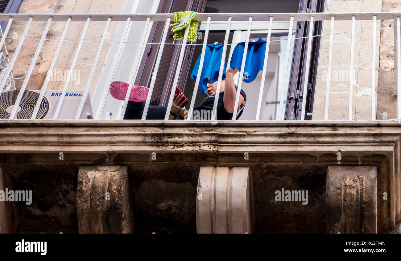 Persona seduta sul balcone, utilizza lo smartphone, faccia oscurata da appendere, lavaggio a basso angolo di visione, Ortigia, Siracusa, Sicilia, Italia, Europa Foto Stock