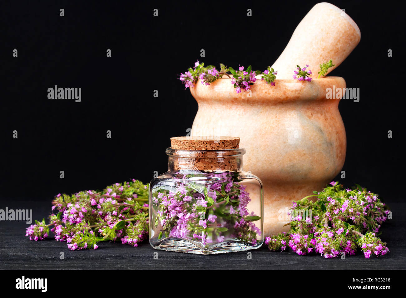 Thymus serpyllum herb in bottiglia. Medicina alternativa concetto su un tavolo di legno su sfondo nero(fuoco selettivo). Foto Stock