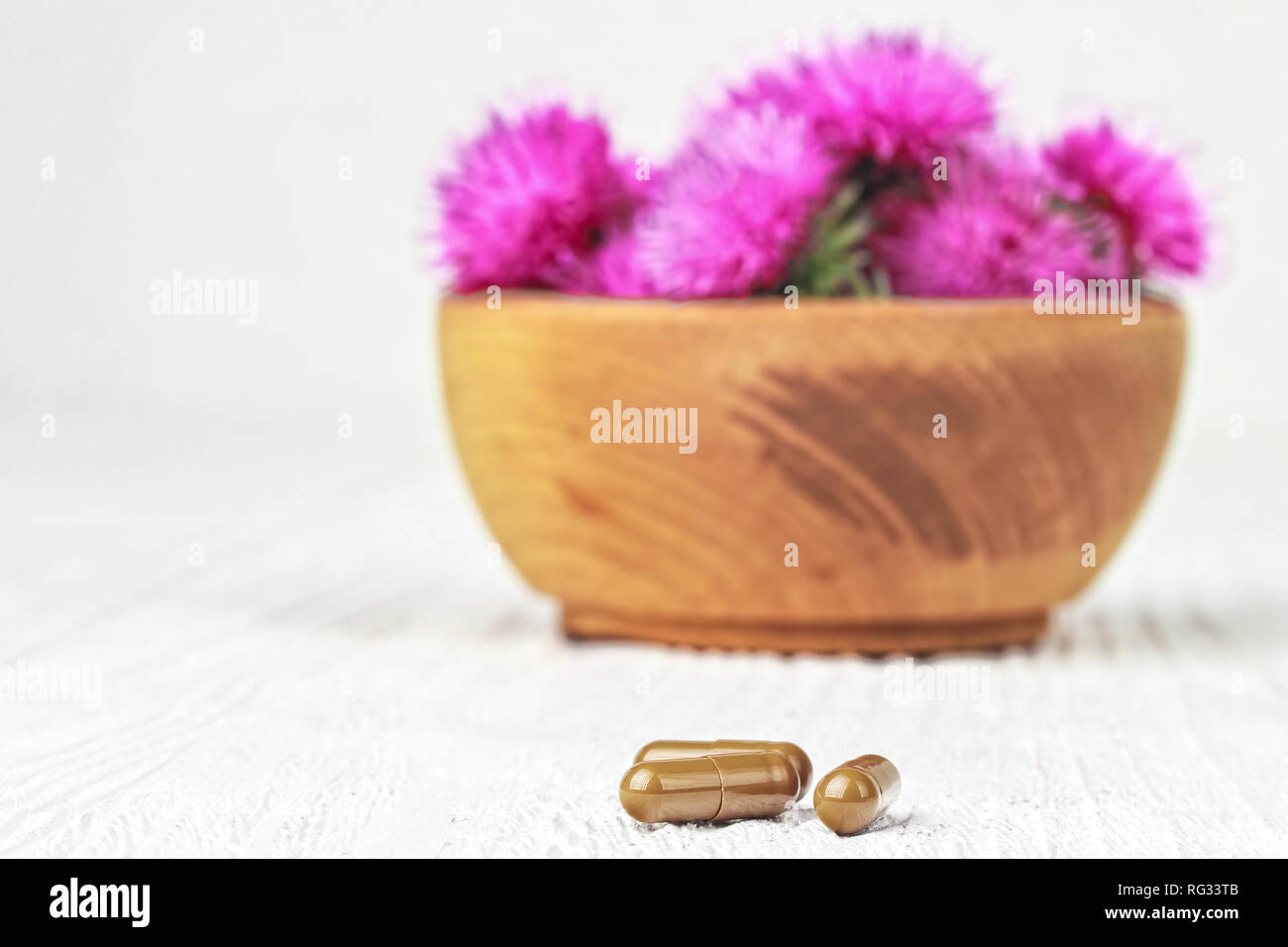 Silybum marianum (cardo) pillole e fiori in un vaso di legno.Uno degli impieghi più comuni di cardo mariano è per trattare problemi di fegato.alternativa Foto Stock