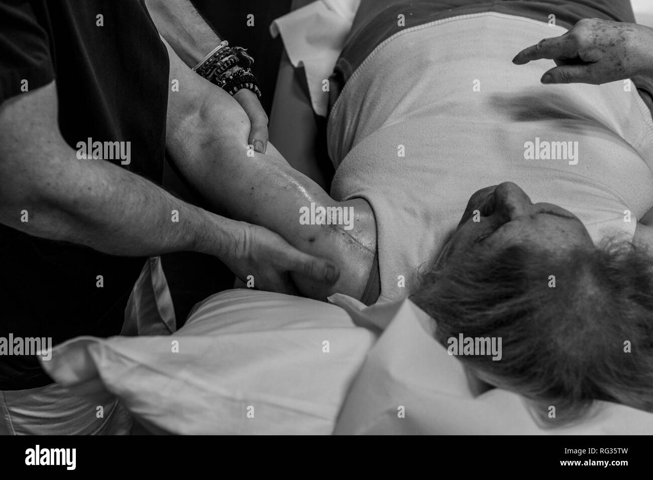 Il fisioterapista Riccardo di Lauro lavorando su una matura donna bianca che presenta una cicatrice sulla sua spalla sinistra, chi è sdraiato sul letto di un ospedale in Foto Stock