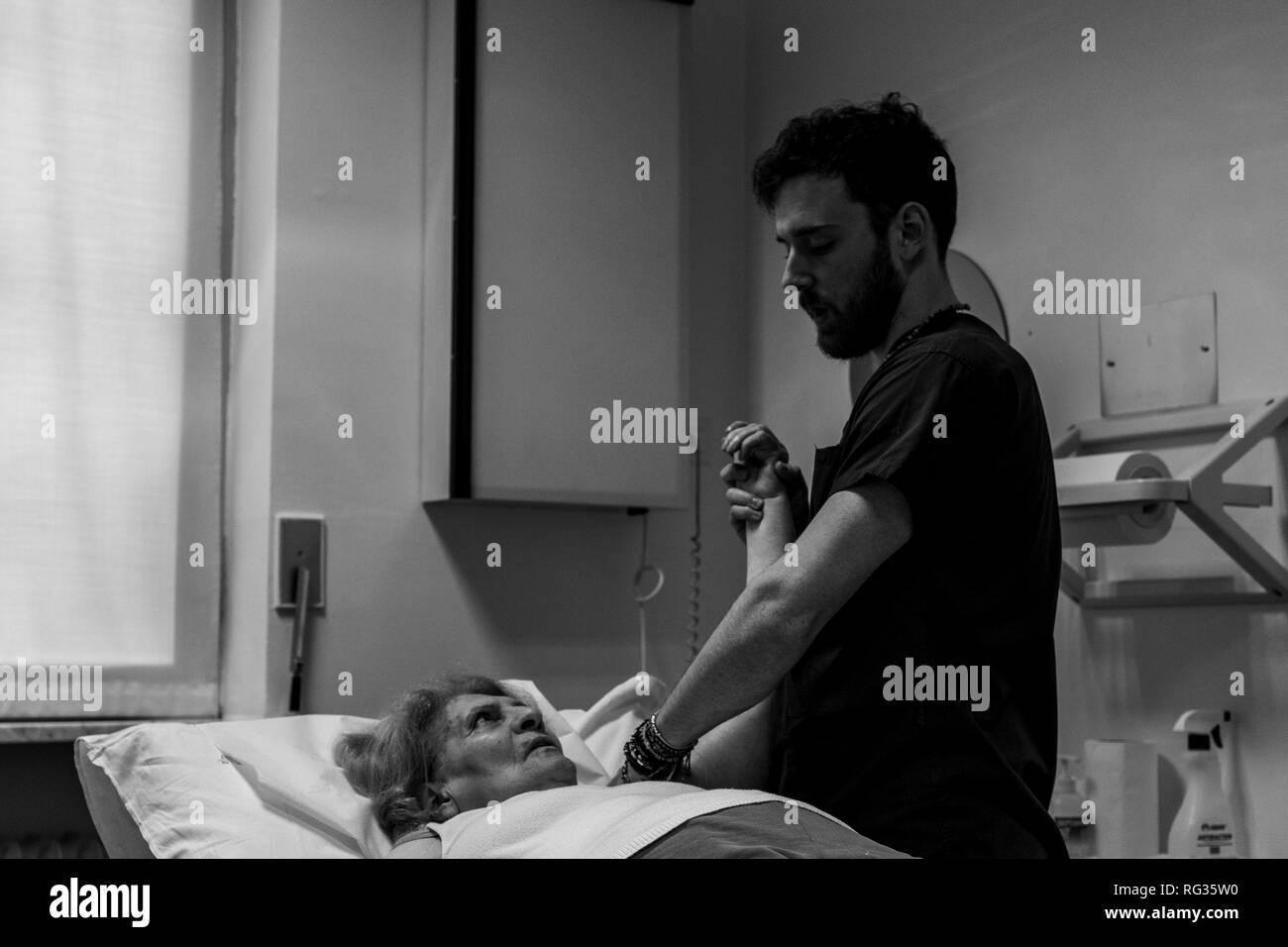 Il fisioterapista Riccardo di Lauro lavorando su una matura donna bianca che presenta una cicatrice sulla sua spalla sinistra, chi è sdraiato sul letto di un ospedale in Foto Stock