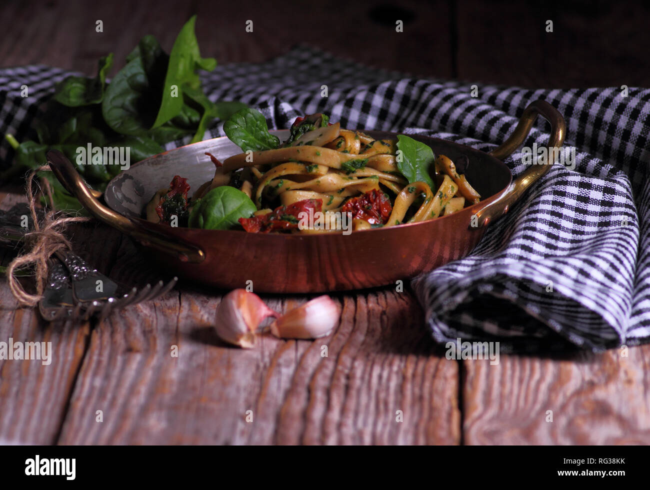 Spaghetti con spinaci e pomodori secchi su di un tavolo di legno. Messa a fuoco selettiva. Foto Stock
