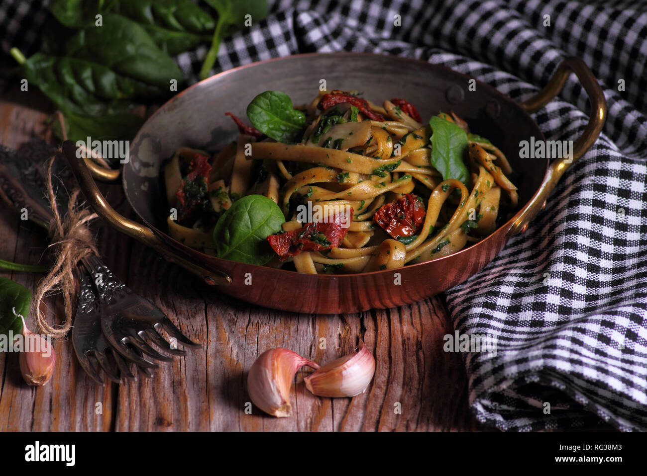 Spaghetti con spinaci e pomodori secchi su di un tavolo di legno. Messa a fuoco selettiva. Foto Stock