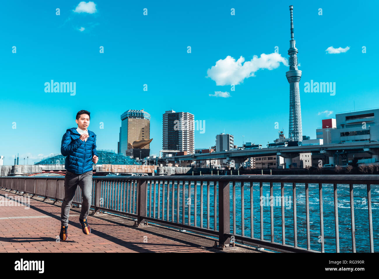 Uomo asiatico esercizio in esecuzione dal fiume Sumida, Tokyo Skytree in background. Allenamento sportivo, uno stile di vita sano, o a Tokyo 2020 Olimpiadi di estate annuncio Foto Stock