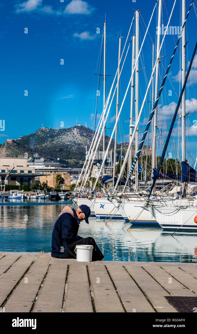 Uomo seduto sul dock in porto, barche ormeggiate in background, della città di Palermo, Sicilia, Italia, Europa Foto Stock