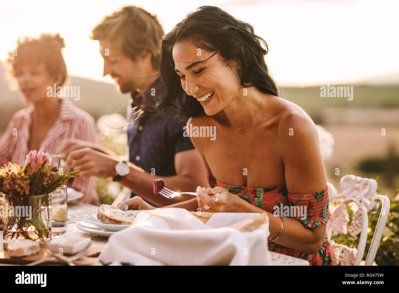 Bella donna mangiare seduti con gli amici ad una festa all'aperto. Donna godendo avente il cibo con gli amici a una festa. Foto Stock