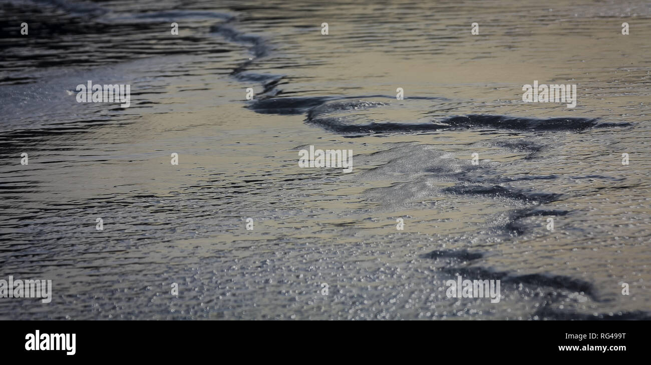 Impostazione sun crea bagliore dorato su ghiaccio e acqua nel fiume a gomito a Kananaskis vicino al torrente di Bragg, Alberta, Canada; calda giornata invernale, Chinook, astratta. Foto Stock