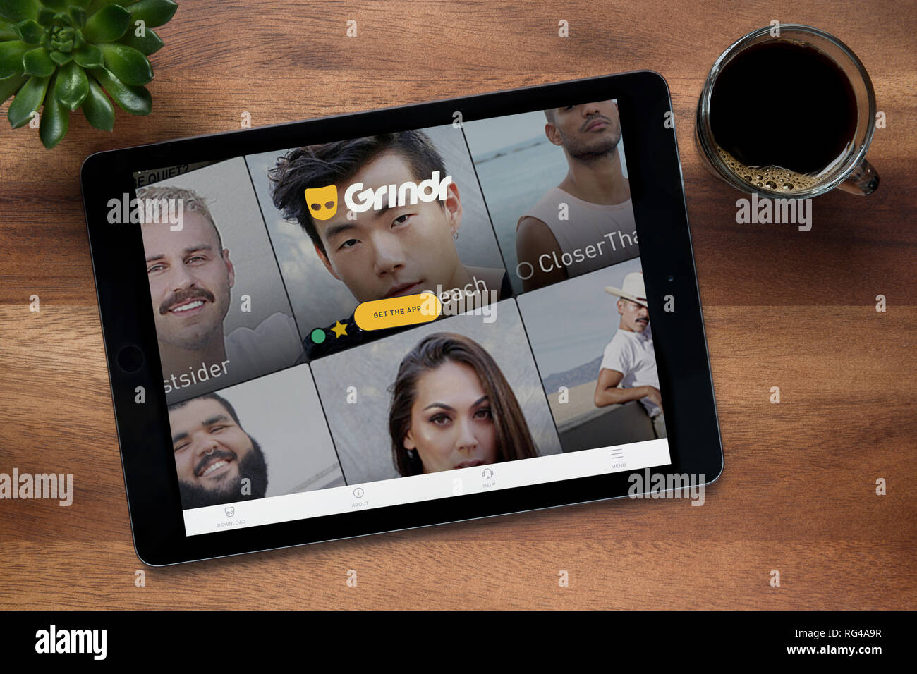 Il sito web di Grindr è visto su un tablet iPad, su di un tavolo di legno lungo con un caffè espresso e una pianta di casa (solo uso editoriale). Foto Stock