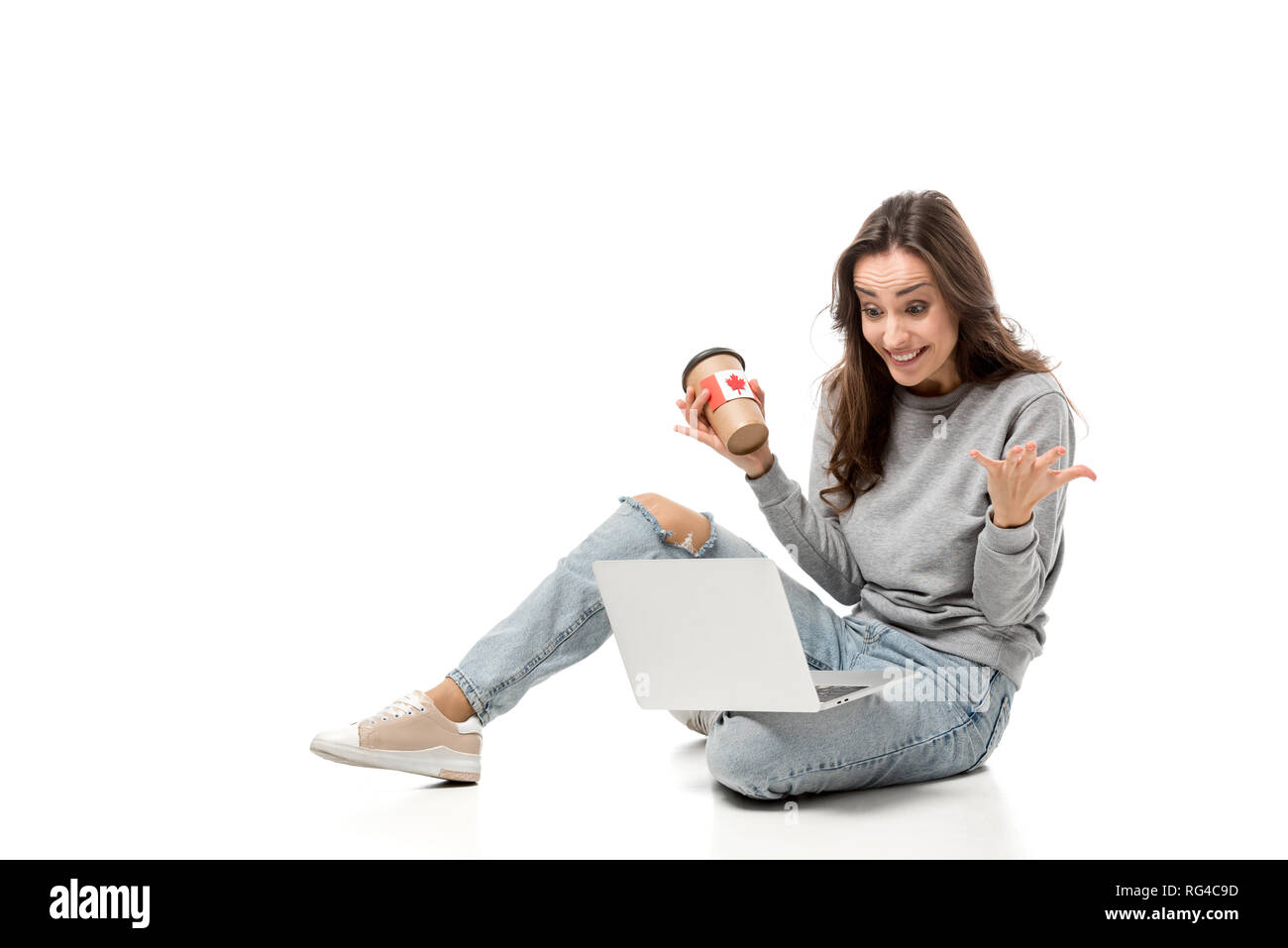 Sorpreso donna utilizzando laptop e azienda tazza da caffè con la bandiera canadese sticker isolato su bianco Foto Stock