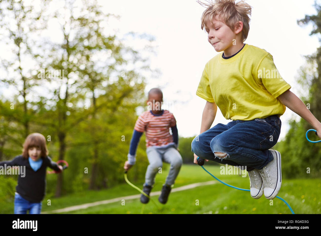 Ragazzo nel parco insieme con gli amici in concorrenza nel salto con la corda in estate Foto Stock