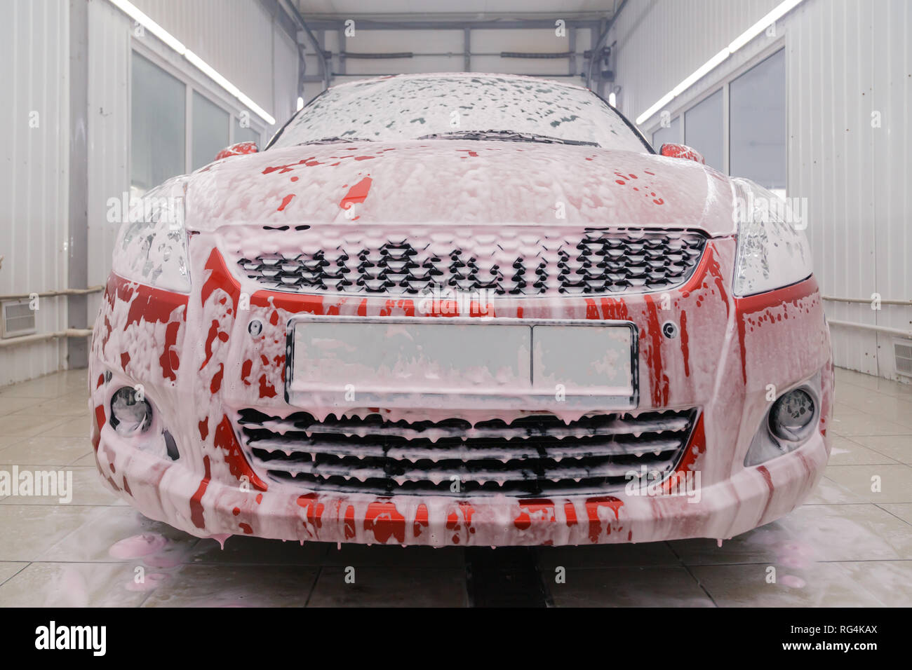 La Russia Kemerovo 2019-01-05 Suzuki Swift rosso brillante piccola auto a car wash in schiuma bianca, professional detergenti chimici per la pulizia automatica. Concetto com Foto Stock