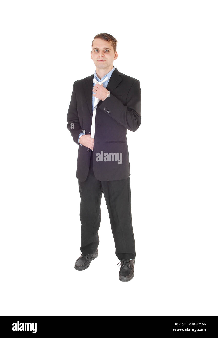 Un bel giovane uomo in piedi dalla parte anteriore è un abito scuro e camicia blu fissa il suo tirante, isolato per sfondo bianco Foto Stock