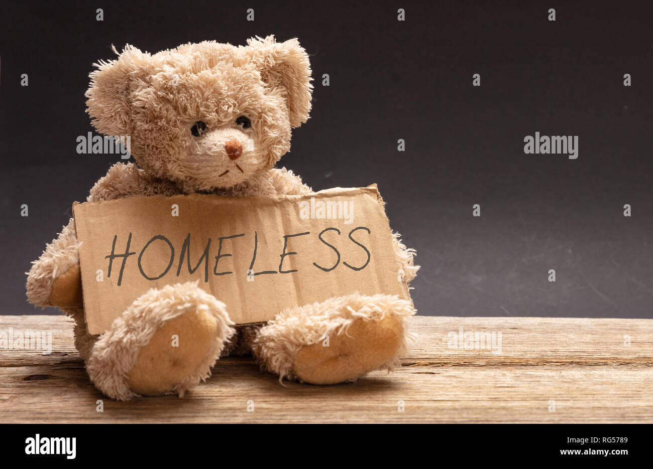 Bambini senzatetto concetto. Orsacchiotto triste, tenendo in mano un cartello di cartone, testo senzatetto, sfondo nero Foto Stock
