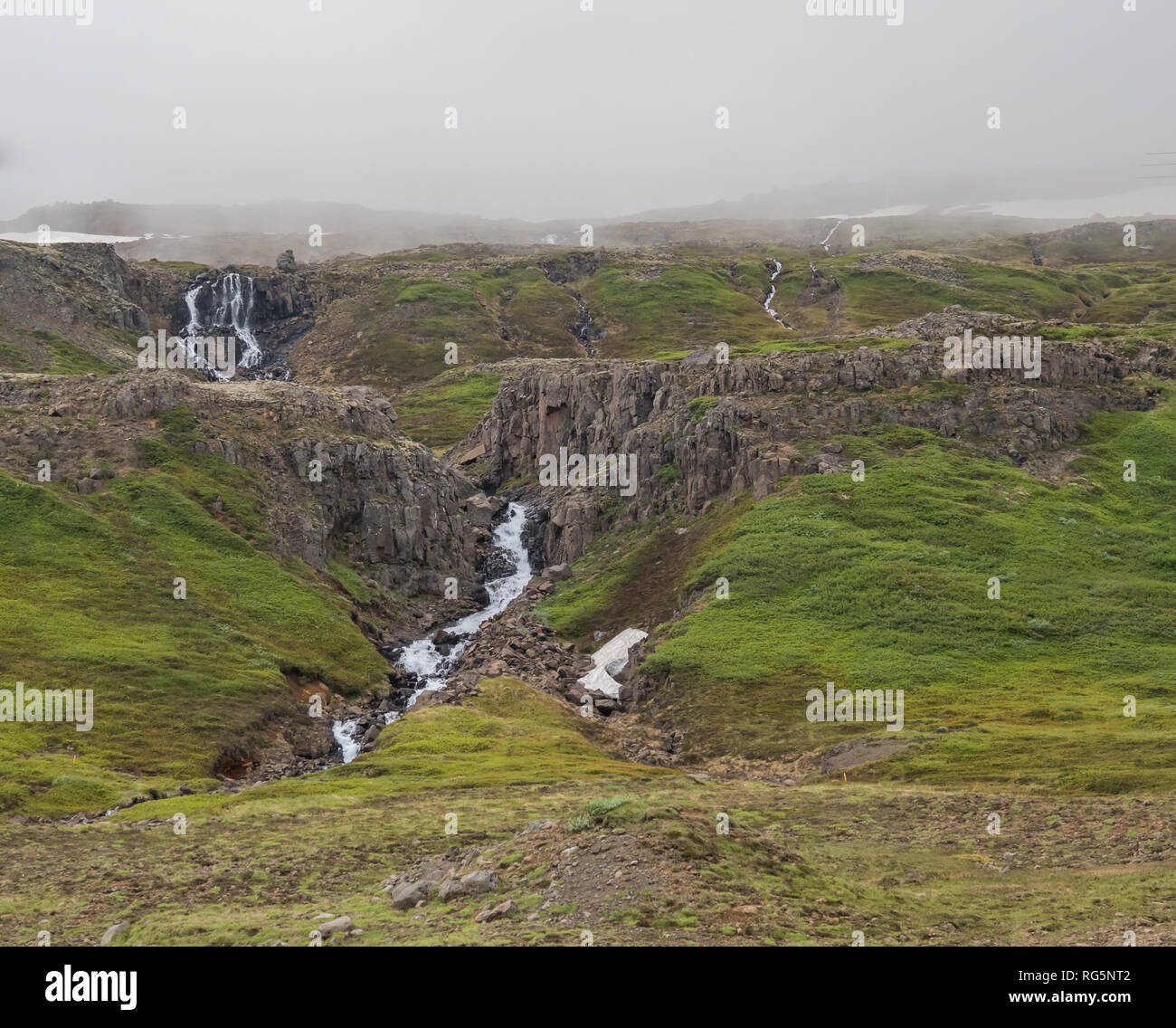Scenario stradale vicino circostante: Seyðisfjörður, Islanda, dove le cascate emergono dai ghiacciai sulle cime di nebbia prima di tumbling attraverso il paesaggio roccioso Foto Stock