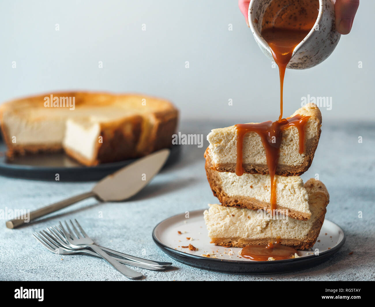 Caramello versando sulla pila di tre pezzi cheesekace. Cheesecake con caramello sul cemento grigio Sfondo. Copia spazio per il testo. Foto Stock