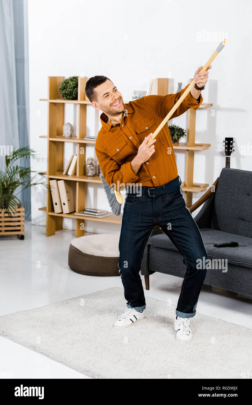 Uomo bello ballare con la scopa in soggiorno moderno Foto Stock