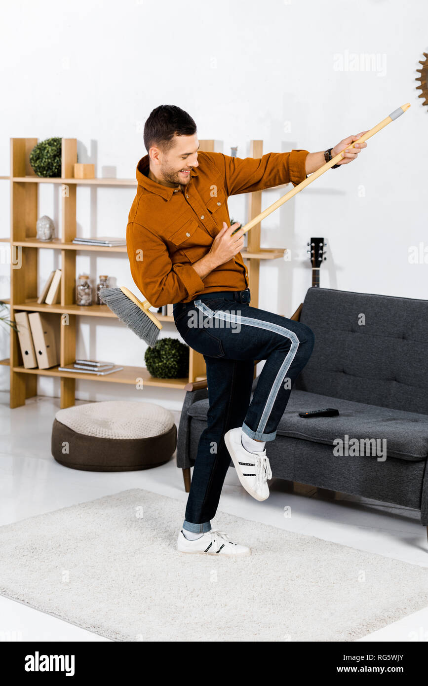 Allegro uomo ballando con la scopa in soggiorno moderno Foto Stock