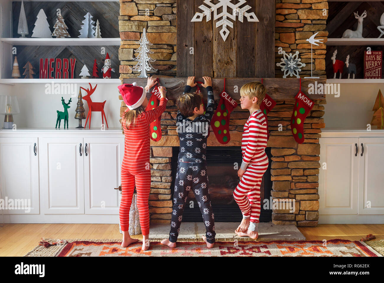Tre bambini appendere le calze di Natale su un caminetto Foto Stock