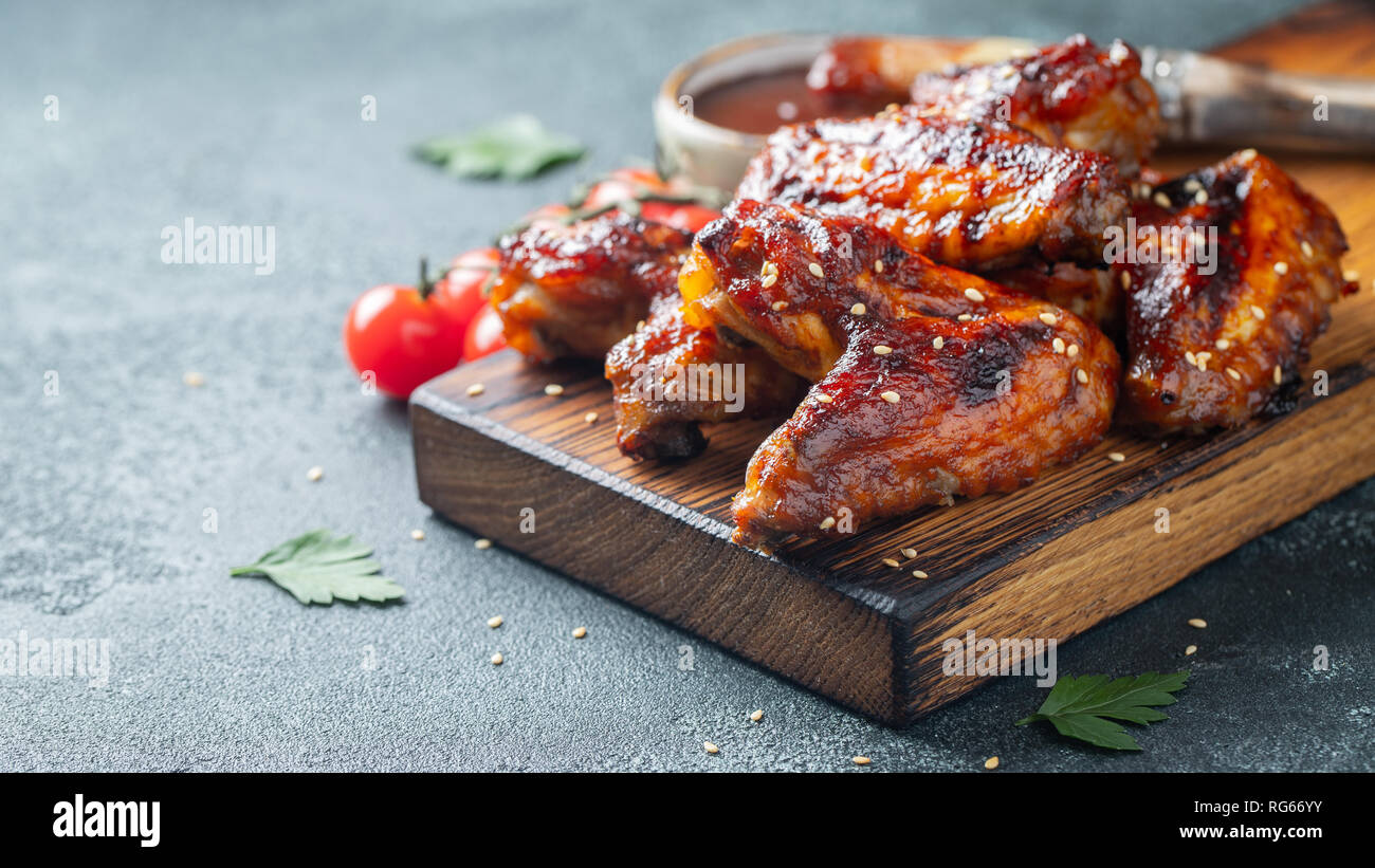 Arrosto di ali di pollo in salsa barbecue con semi di sesamo e prezzemolo su una tavola di legno su una tavola di calcestruzzo. Con copia spazio. Gustosi snack per la birra per Foto Stock