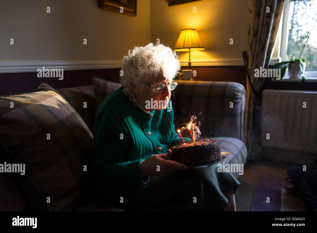 Donna anziana festeggia il suo compleanno con una torta mentre soffiando fuori le candele, England, Regno Unito Foto Stock