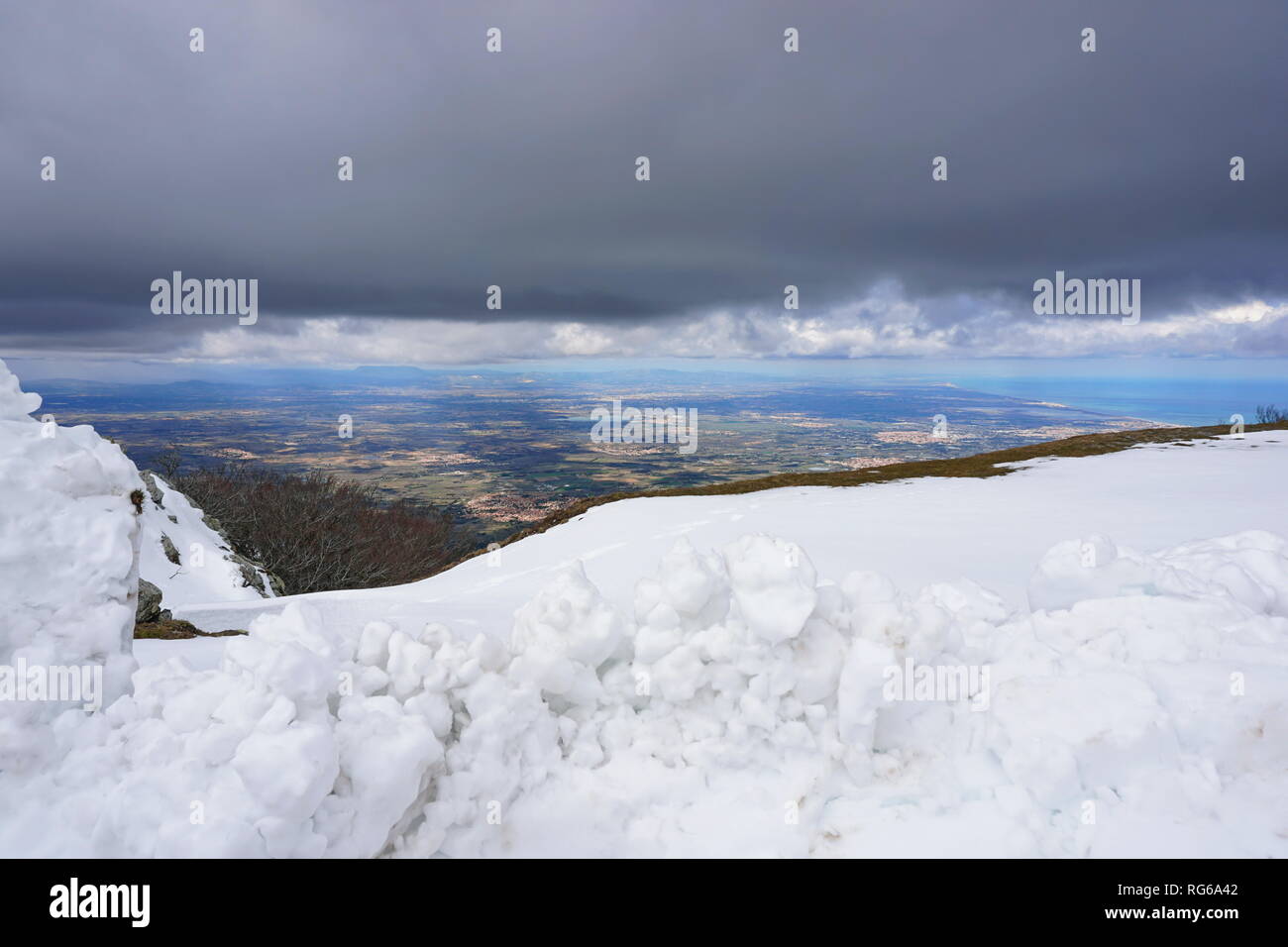 La Francia vista sulla pianura di Rossiglione con neve in primo piano e cielo nuvoloso, Massif des Alberes, Pirenei Orientali Foto Stock