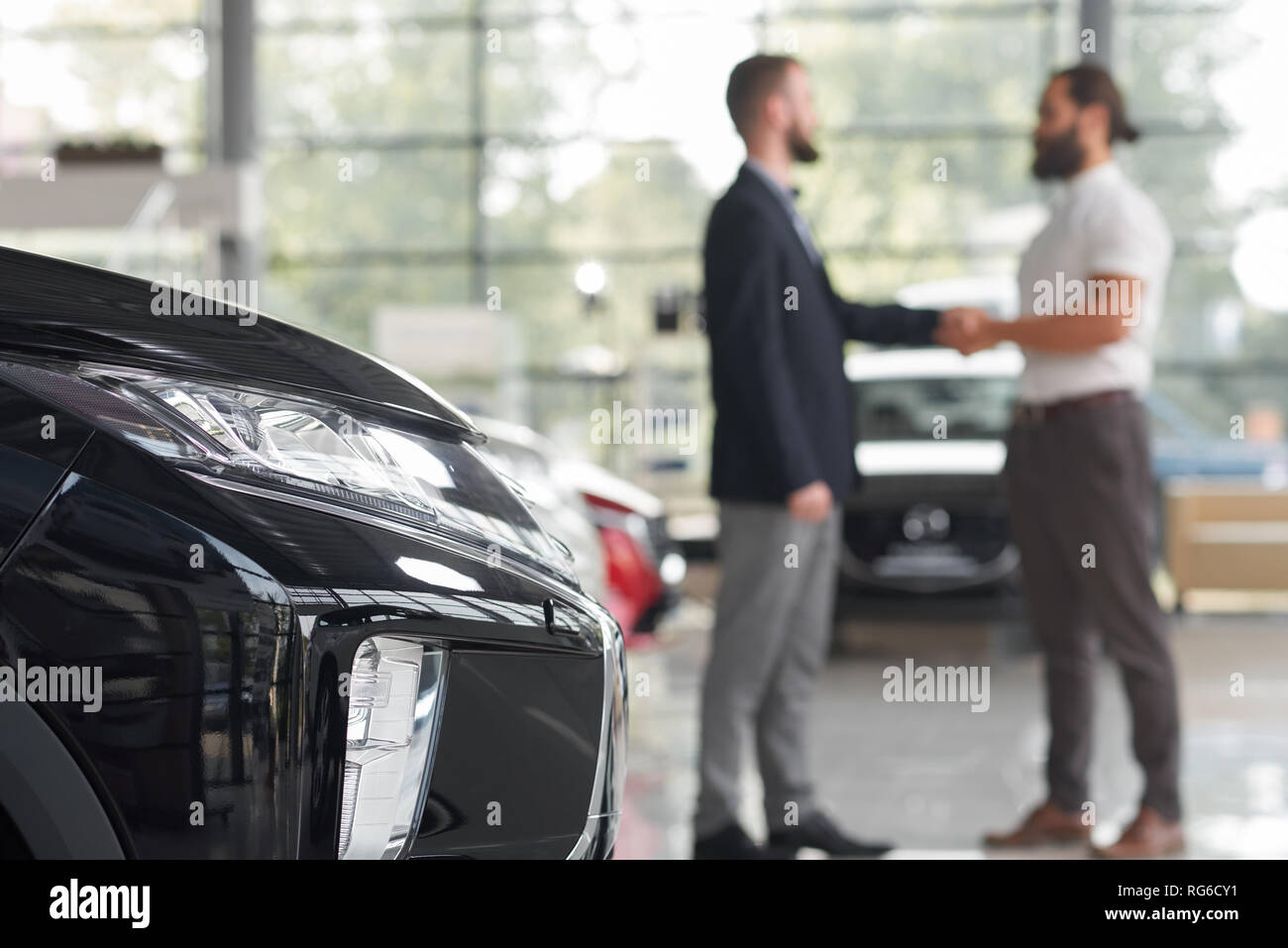 Irriconoscibile uomini stringono le mani, piedi in auto moderna showroom. Nero auto faro. Rivenditore di auto e il cliente del centro di auto rendendo trattativa. Client l'acquisto di un nuovo veicolo. Foto Stock