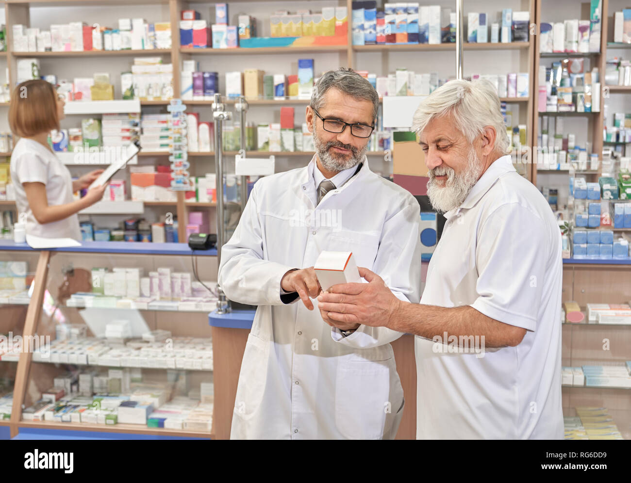Medico la scelta di farmaci con paziente in farmacia. Specialista professionale aiutando uomo anziano con medicamenti. Titolare di pensione o di rendita azienda cassetta medica. Il farmacista in piedi vicino a ripiani con farmaci. Foto Stock