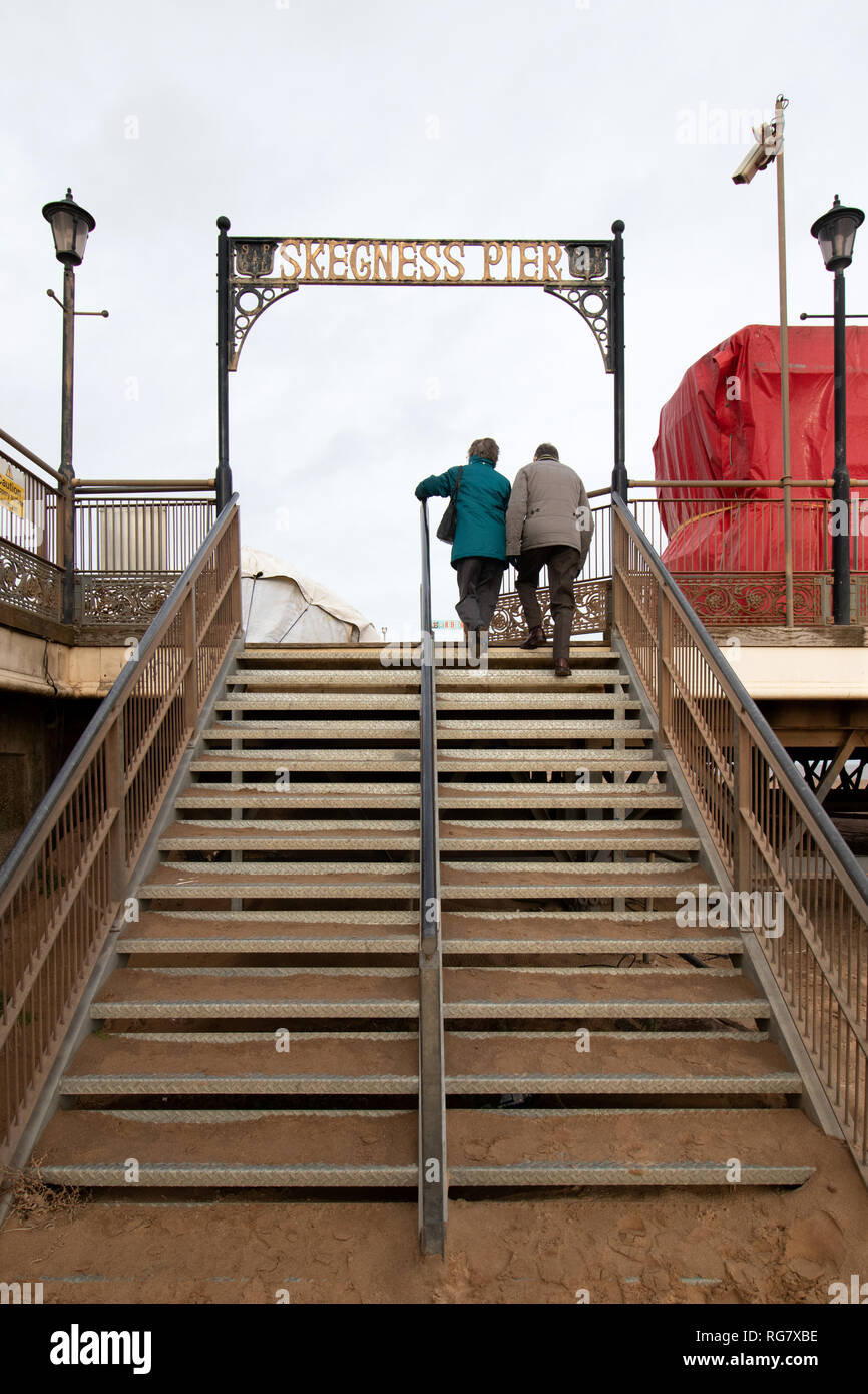 Due persone che salgono i gradini di sabbia che portano a skegness pier Foto Stock