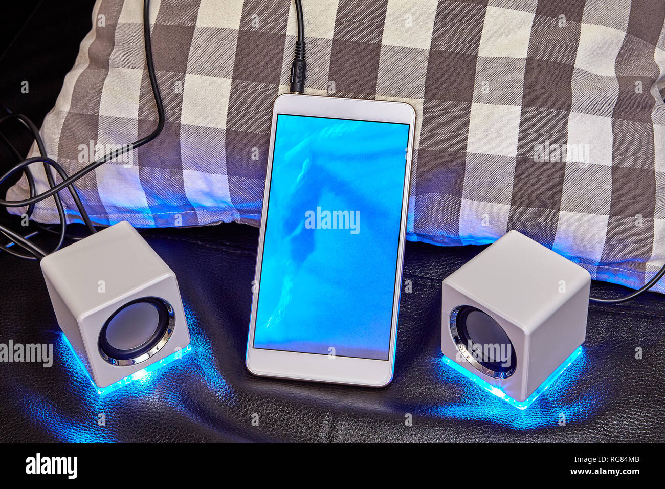 Uno smartphone con un display blu è collegato al mini altoparlanti con un cavo. Foto Stock