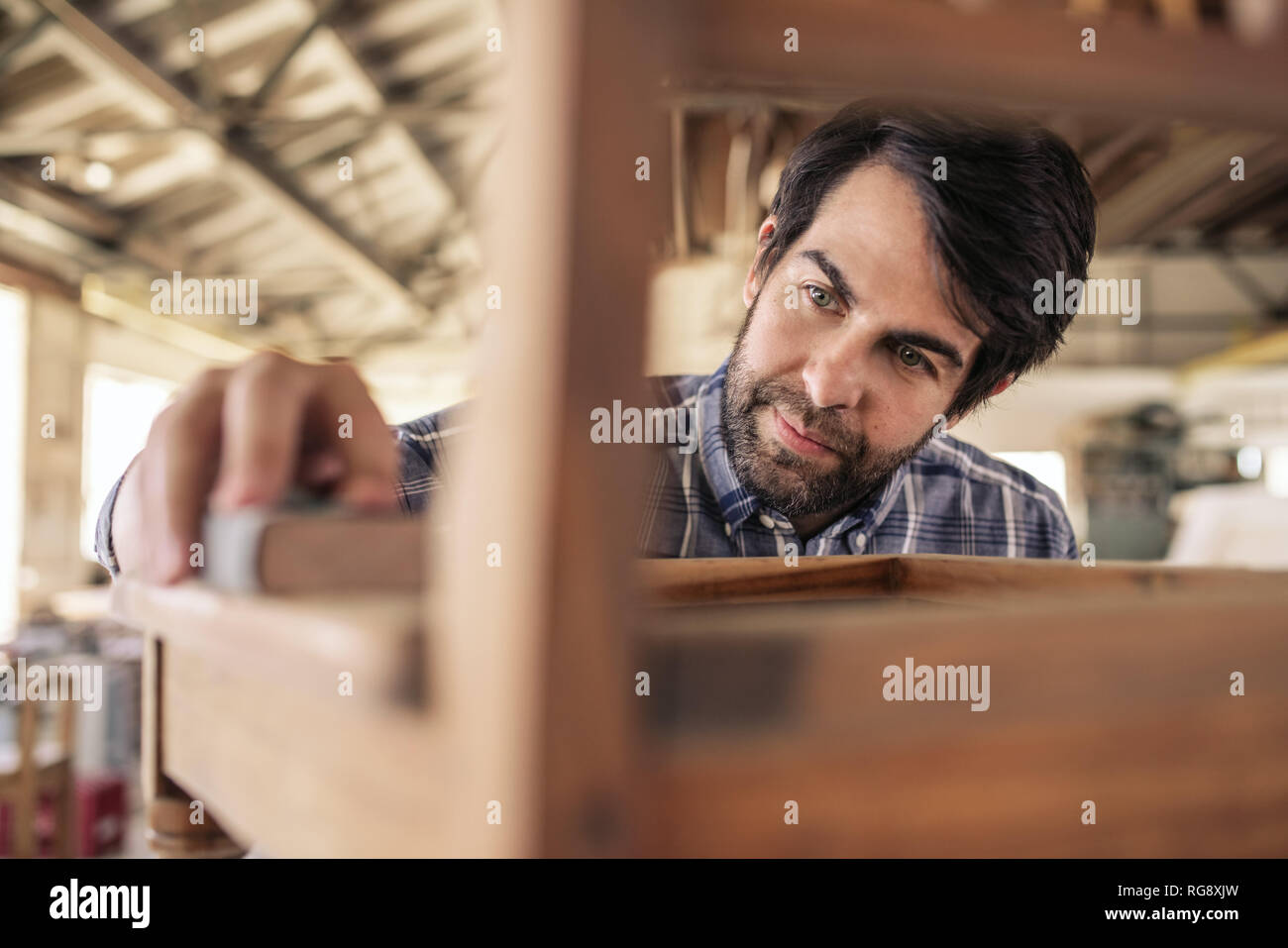 Falegname la levigatura di una sedia nella sua fabbricazione di mobili workshop Foto Stock