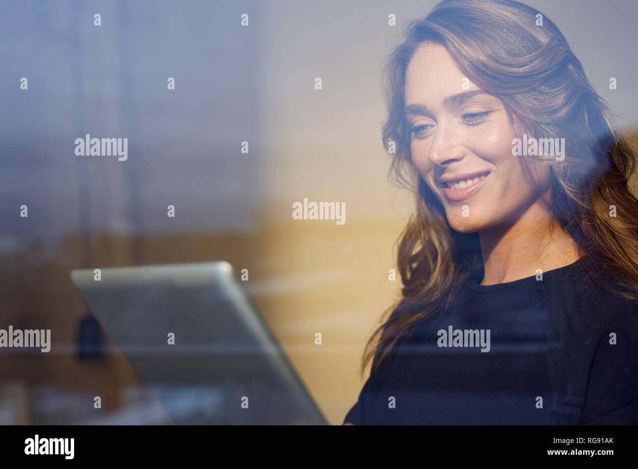 Ritratto di donna sorridente dietro il vetro di finestra utilizzando tablet Foto Stock