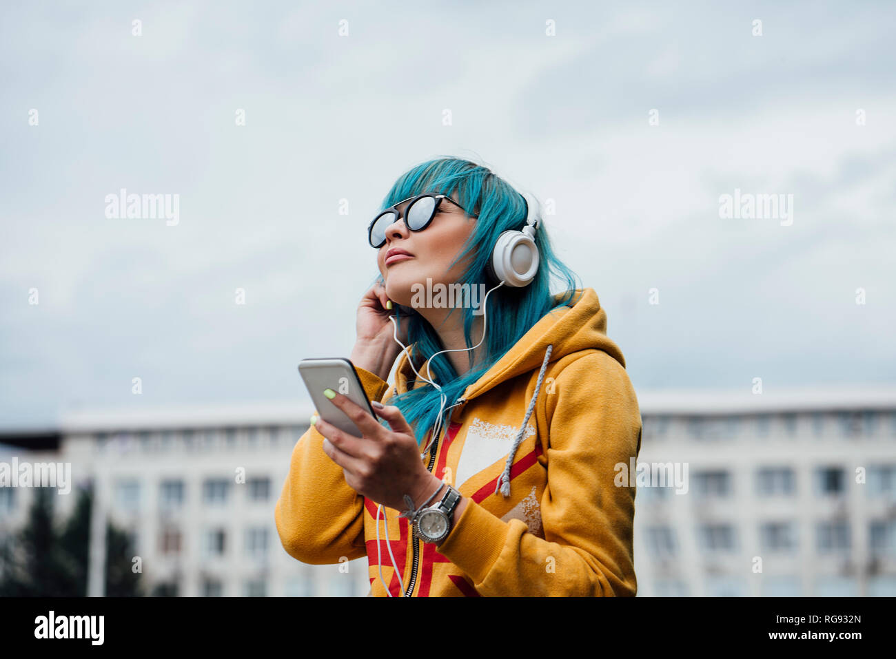 Ritratto di giovane donna con tinti di blu capelli ascoltando musica con lo smartphone e le cuffie Foto Stock